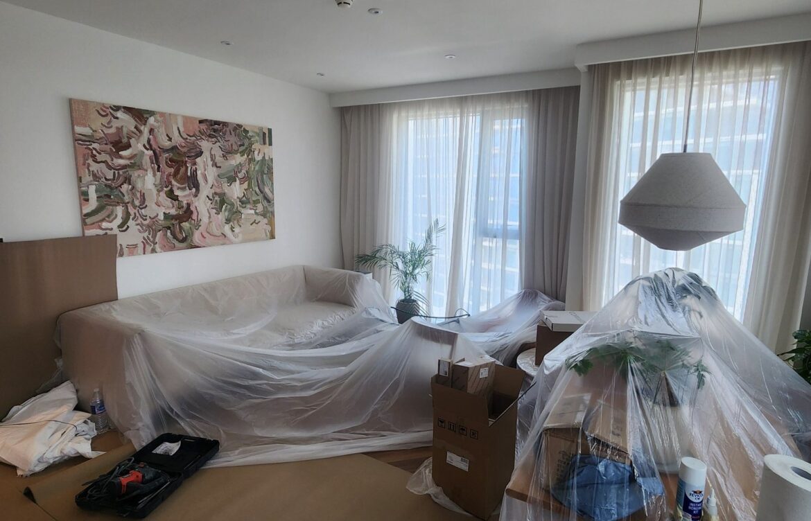Preparing the living room for work: furniture and decor are carefully covered with protective film, and the floor is lined with heavy cardboard