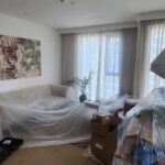 Preparing the living room for work: furniture and decor are carefully covered with protective film, and the floor is lined with heavy cardboard