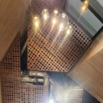 Looking up into a high entrance hall: perforated copper metal ceiling, glass pendants and ducts.