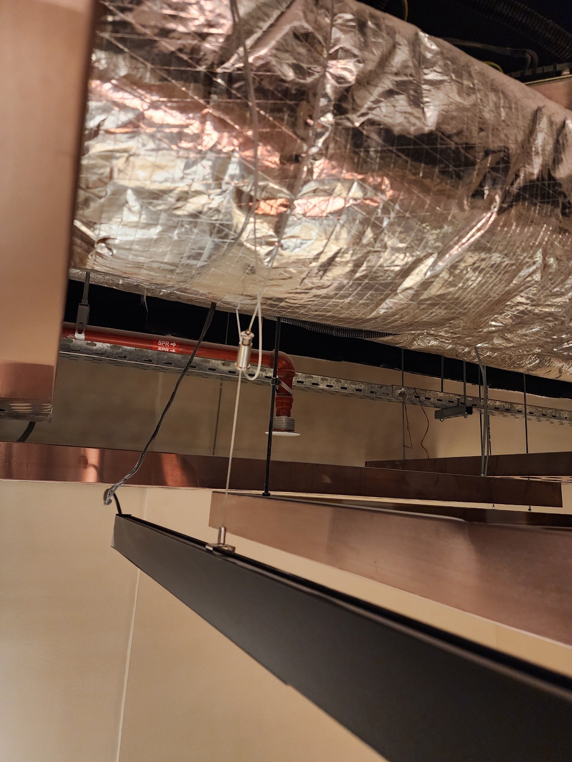Close-up of an insulated duct, sprinkler pipe and the edge of a hanging metal ceiling.