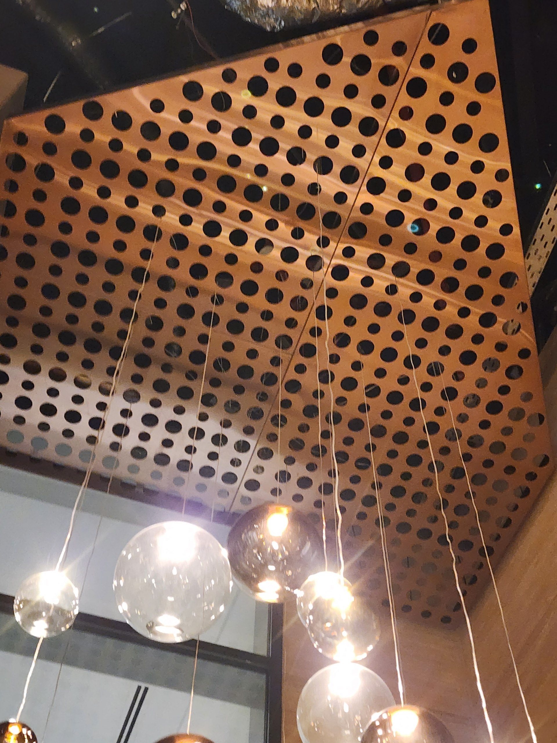 Glass pendant lights passing through a perforated copper ceiling panel.